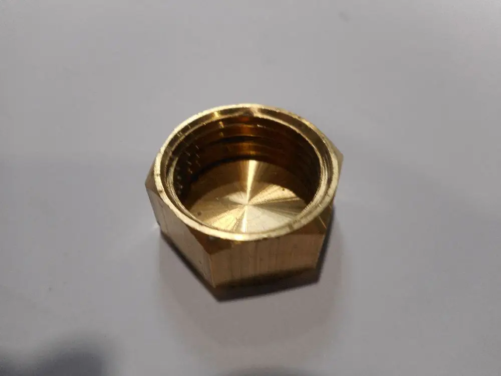 Brass nut, likely from Remeha, featuring internal threading and a hexagonal shape, placed on a light-colored surface.